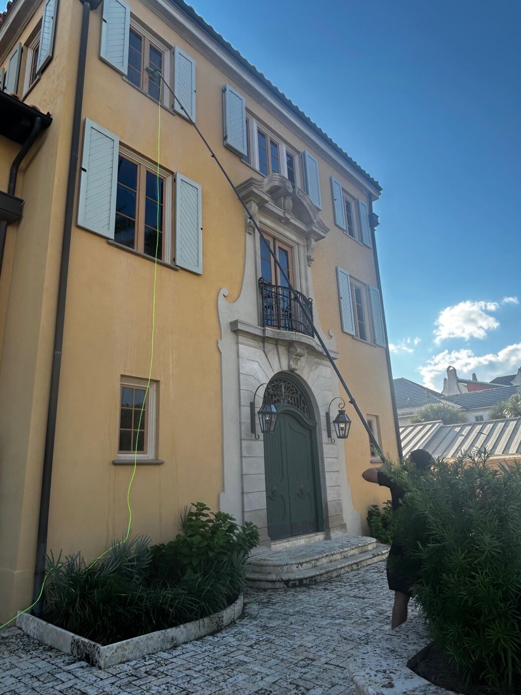Technician using a water-fed pole to clean upper-story windows on a large Mediterranean-style home